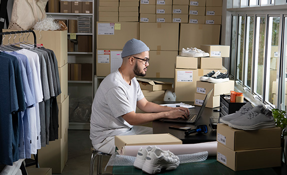 E-commerce male business owner working on laptop computer in store warehouse.